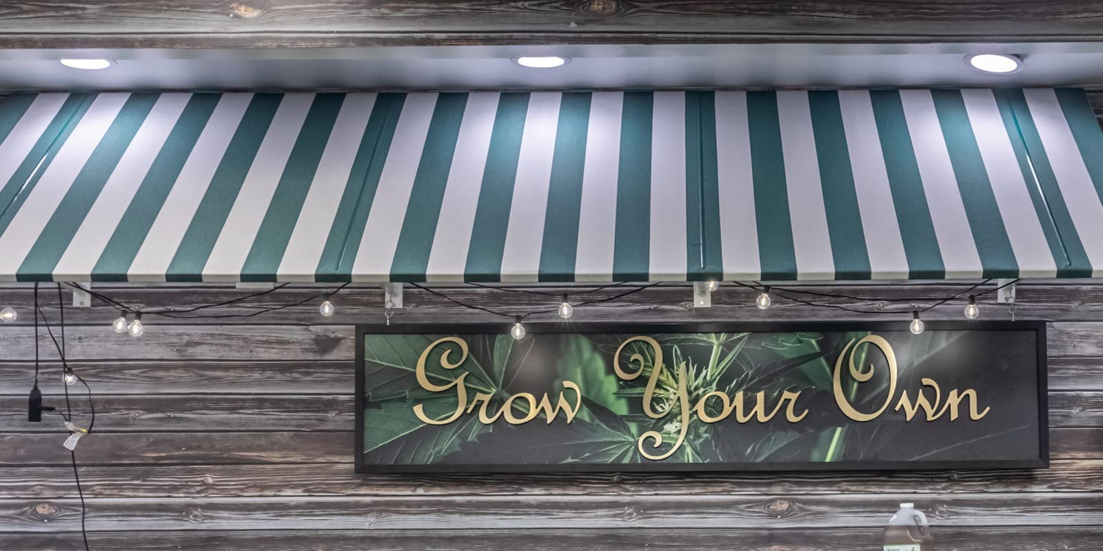 The Grow Your Own sign at Farmers Choice Fishkill, gold script over a cannabis-leaf backdrop under a green and white striped awning on weathered barn board walls