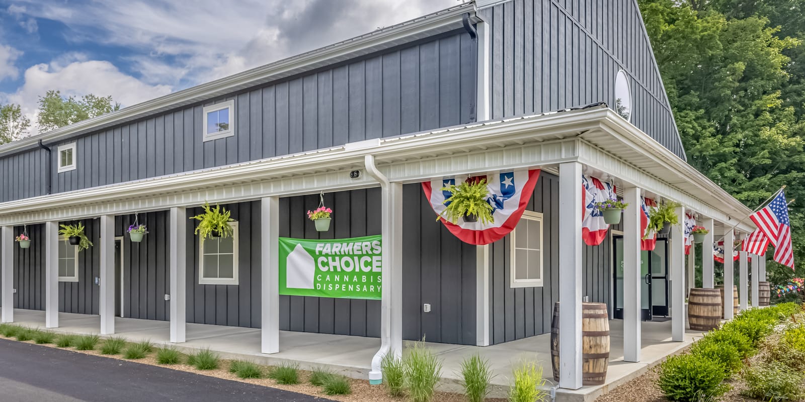 The side porch of the Farmers Choice barn in New Paltz, white columns, hanging ferns and red, white and blue bunting, with the store's green sign on the wall
