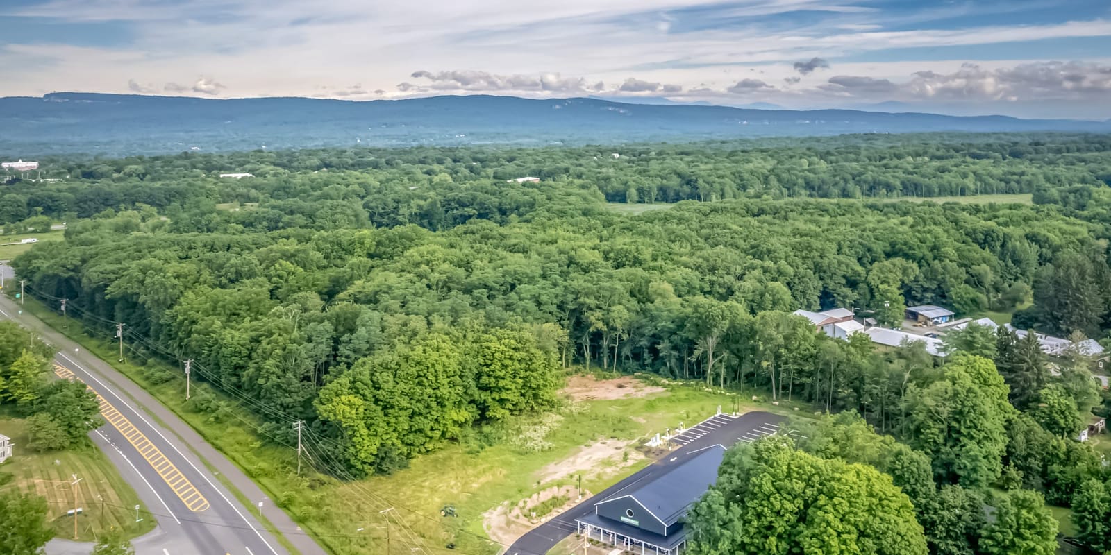 Aerial view over New Paltz toward the Shawangunk Ridge, Route 299 running through the trees with the Farmers Choice barn small at the roadside