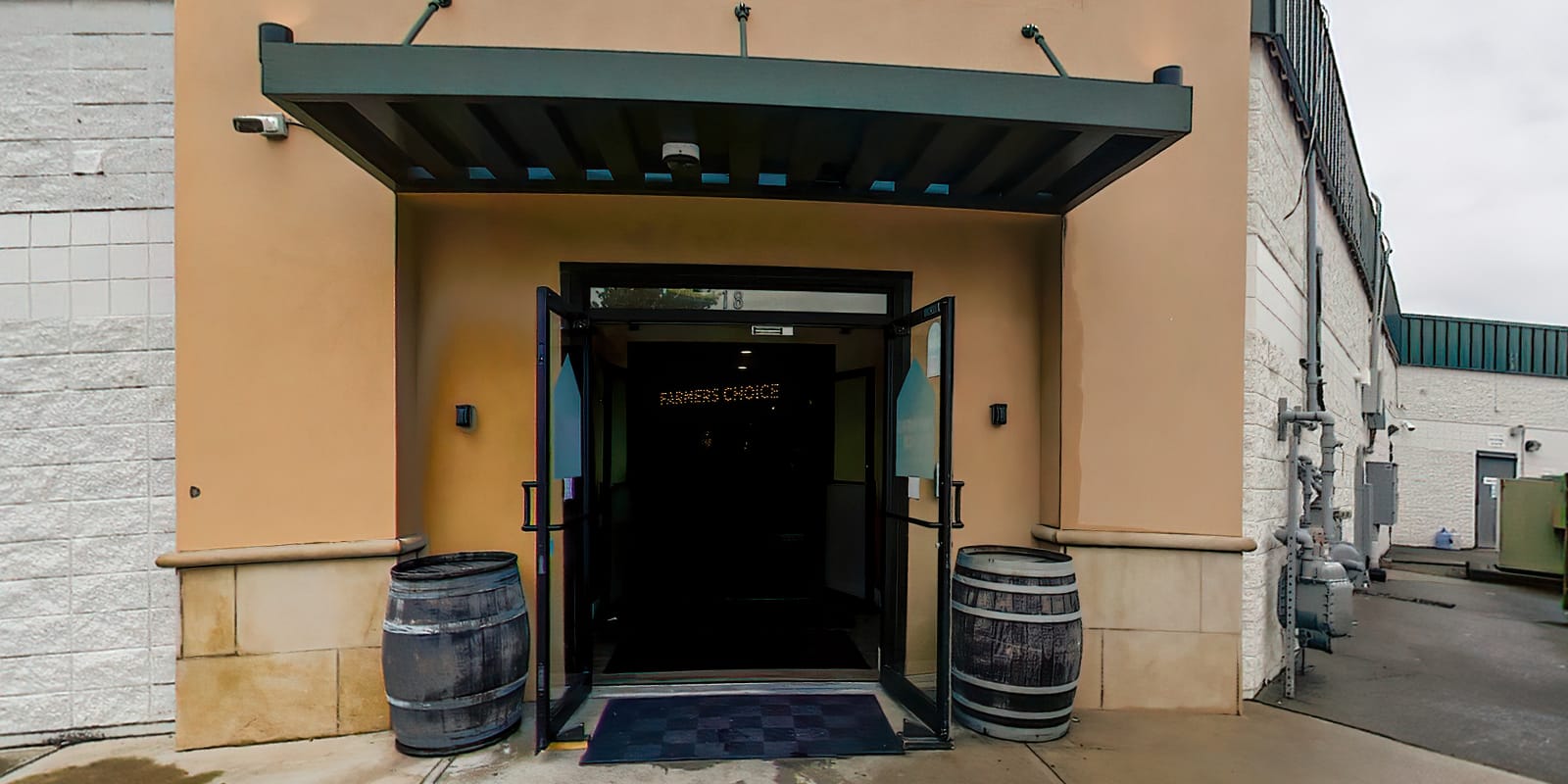 The entrance of Farmers Choice Fishkill up close, glass doors under a dark awning with an oak barrel on each side