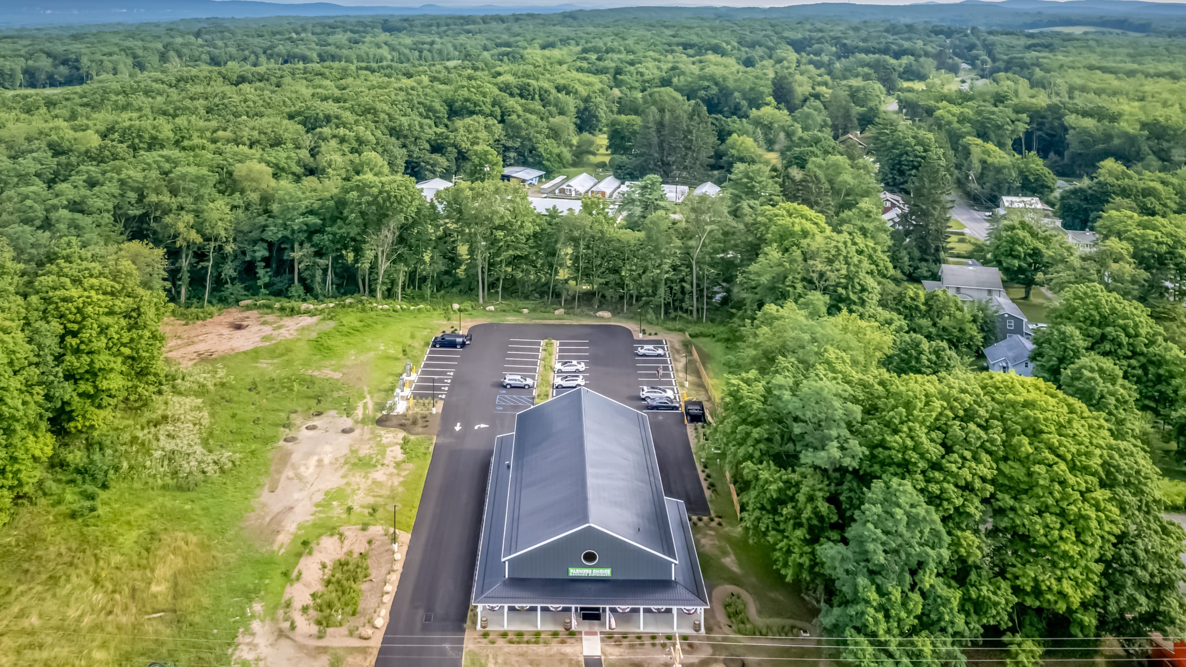 The Farmers Choice New Paltz barn from above, its gray metal roof set among summer trees with the ridge on the horizon