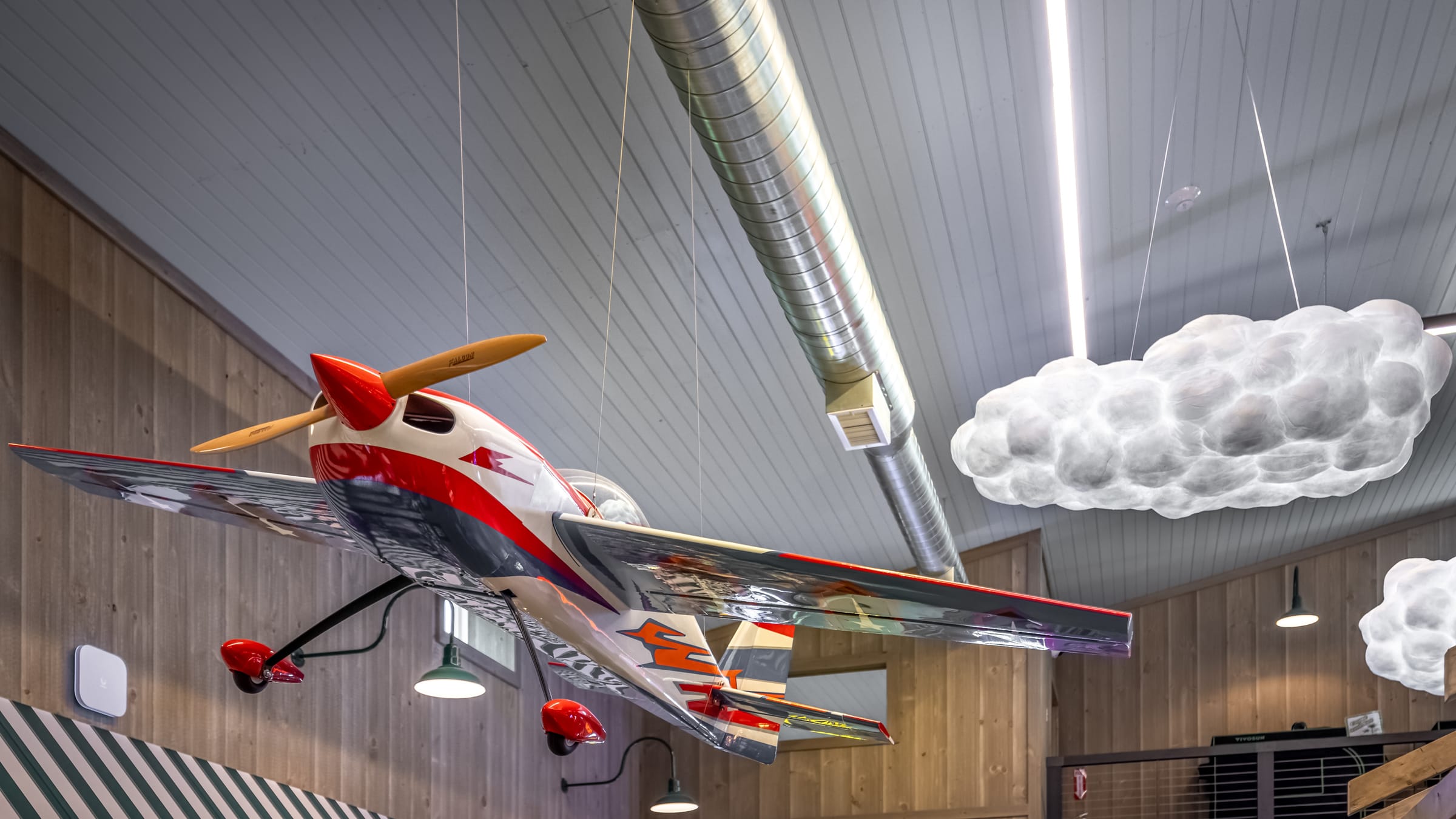 A red and white model airplane and a cloud-shaped lamp hanging from the wooden ceiling of the Farmers Choice New Paltz barn