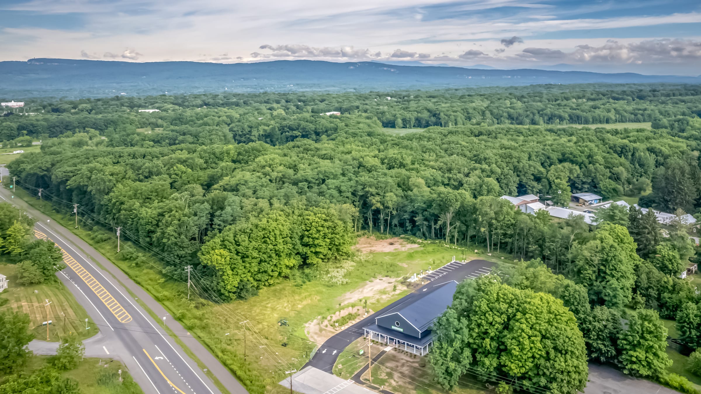 Aerial view over New Paltz toward the Shawangunk Ridge, Route 299 running through the trees with the Farmers Choice barn small at the roadside